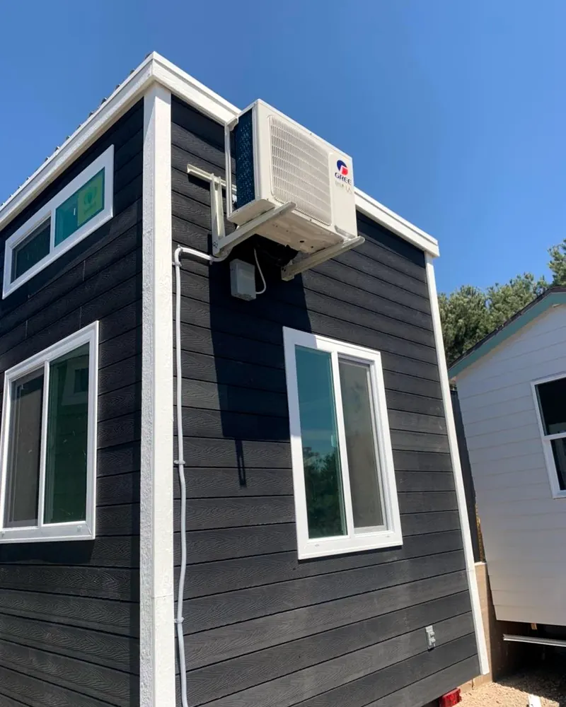 Ductless mini-split outdoor unit mounted high on the wall of a backyard ADU with dark siding