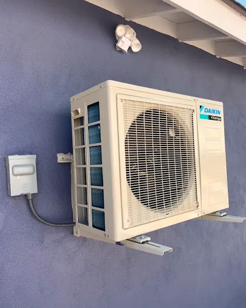 Daikin mini-split outdoor unit on a wall bracket beside its disconnect box