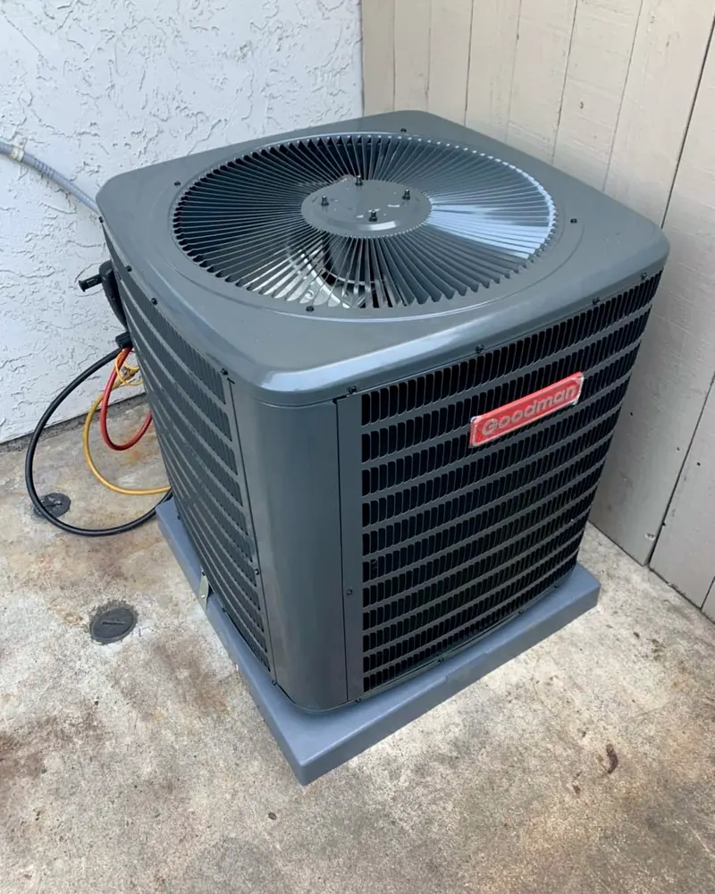 New Goodman outdoor AC unit on a pad in a narrow side yard